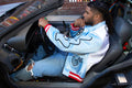 Man in a blue jacket sits in a futuristic car, focused on driving with a thoughtful expression.