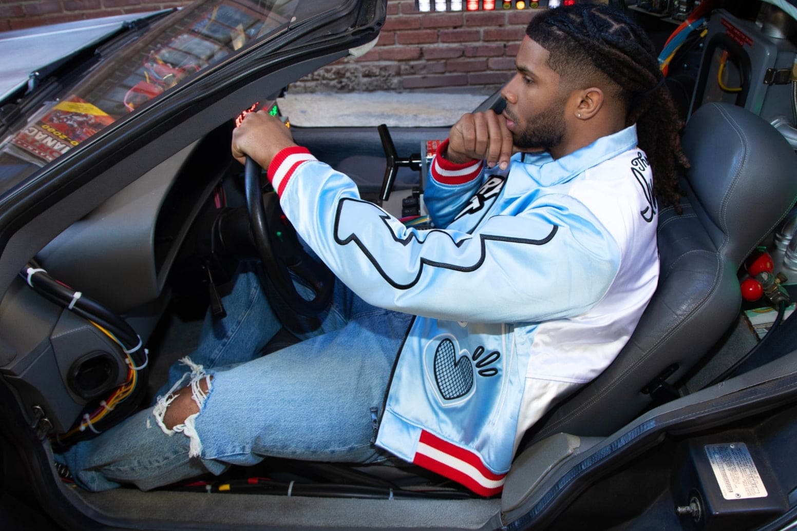 Man in a blue jacket sits in a futuristic car, focused on driving with a thoughtful expression.